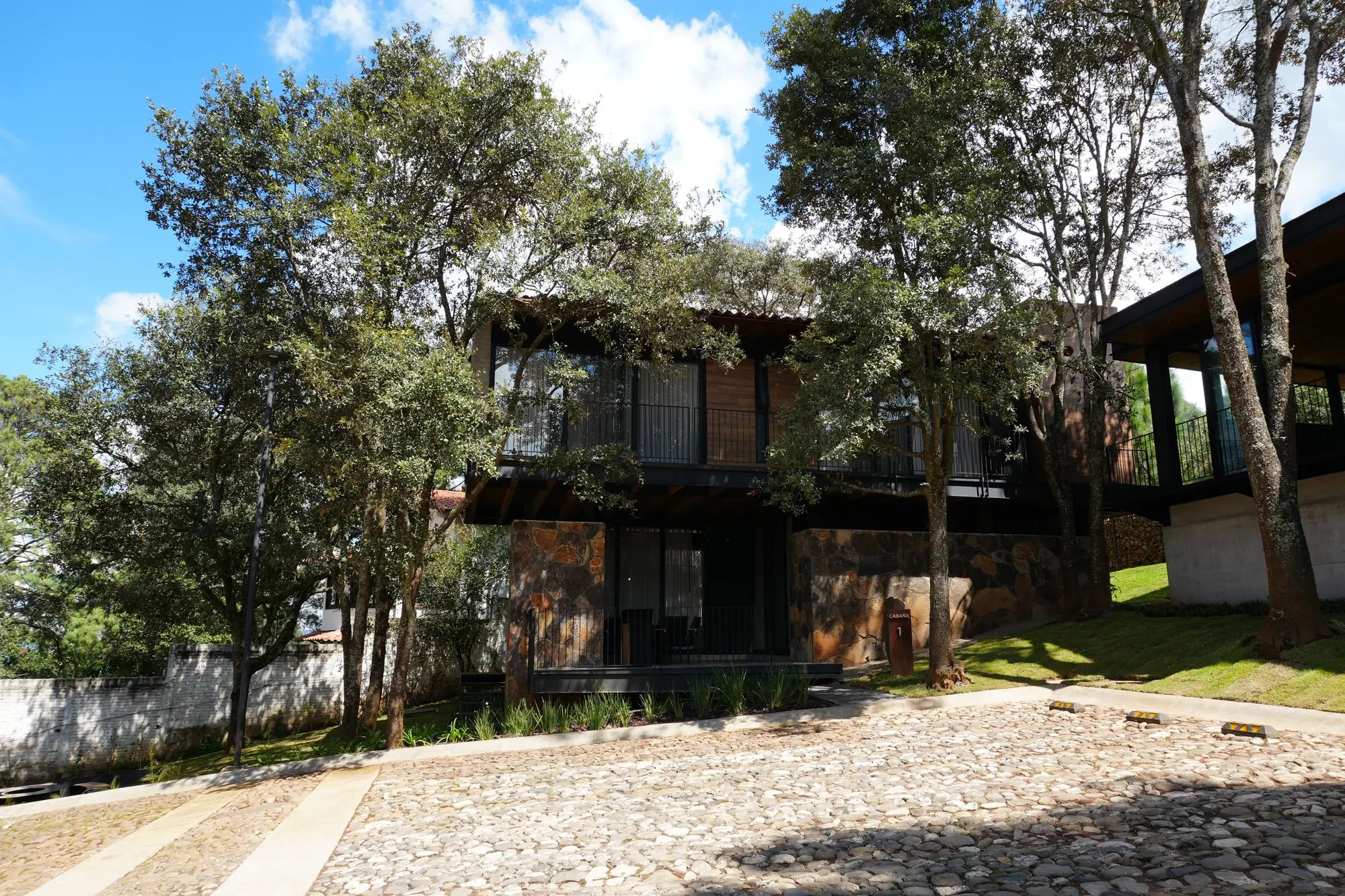 Casa de piedra y madera entre árboles, con patio empedrado